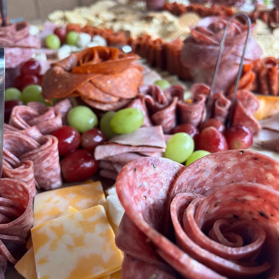 Close-up of an abundant charcuterie platter with sliced meats, cheeses, green and red grapes, olives, and vegetables.